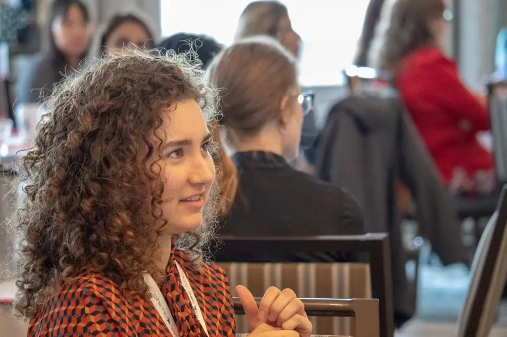 Woman in foreground with people sitting in a conference room blurred out