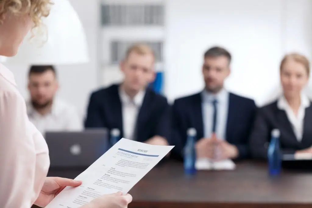 Woman holding resume with men and woman sitting at table in background blurred out