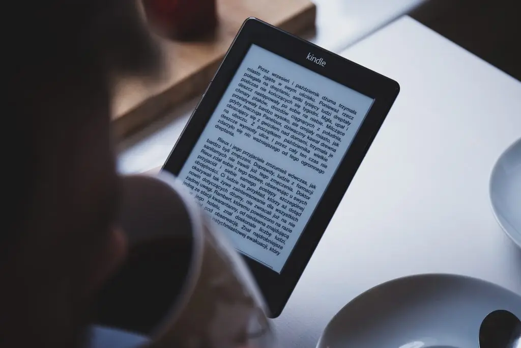 Person reading a book on a tablet taking a sip of coffee