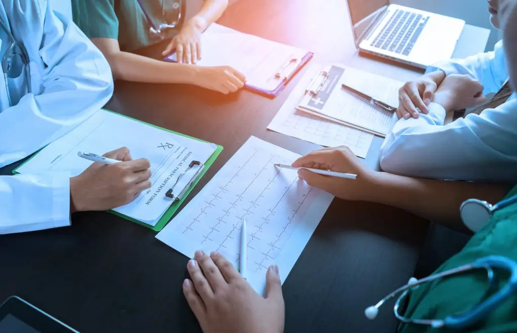 medical team having a meeting with doctors in white lab coats and surgical scrubs seated at a table discussing a patients records,success medical health care, Medicine doctor's working concept