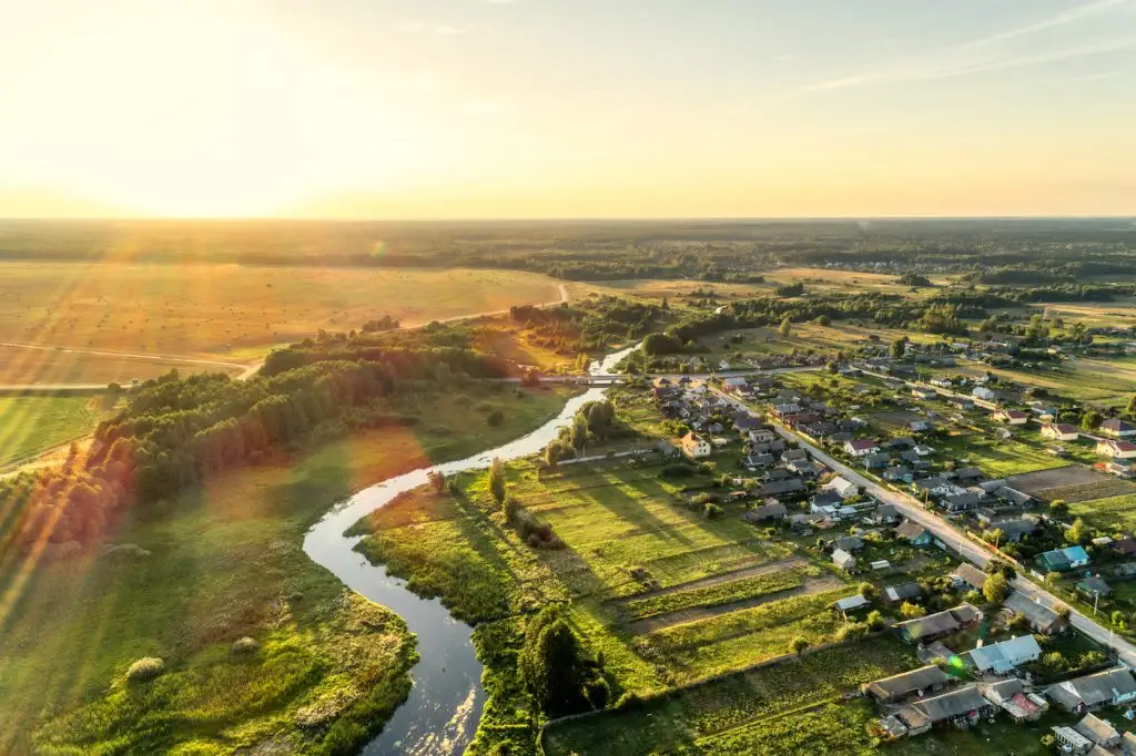 An aerial view of a small village with a blue winding river and farmland on the other side