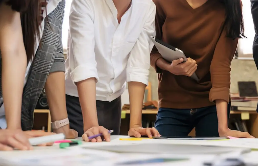 Midsection of business people standing in a room overlooking documents on a table